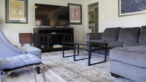 A modern living room with a grey sofa, a glass coffee table, a blue armchair, and a dark entertainment unit.