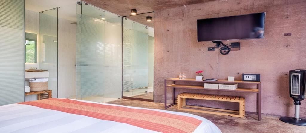 Ein modernes Schlafzimmer mit einem großen Bett, einer Glasdusche, einem Wand-Fernseher und einer Holzbank.