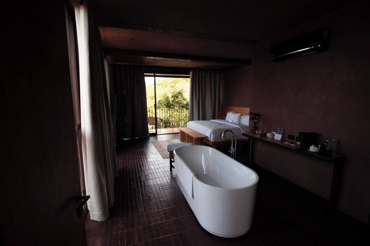 A modern bathroom with a freestanding bathtub, a shower, and a large window offering a view of the outdoors.