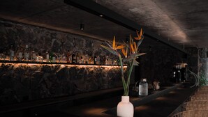 A bar area with a stone wall backdrop, a white vase with plant decorations, and various bottles on the shelf.