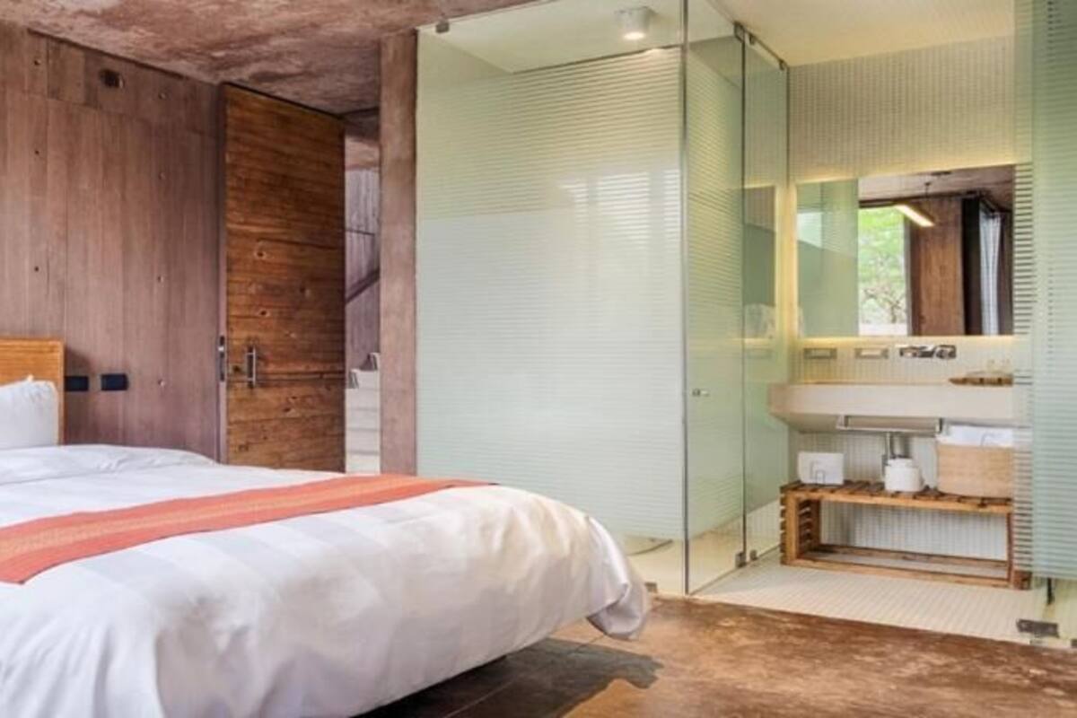 A modern bedroom with a wooden headboard, a large bed with white linens, a glass shower enclosure, and a built-in vanity with a mirror.