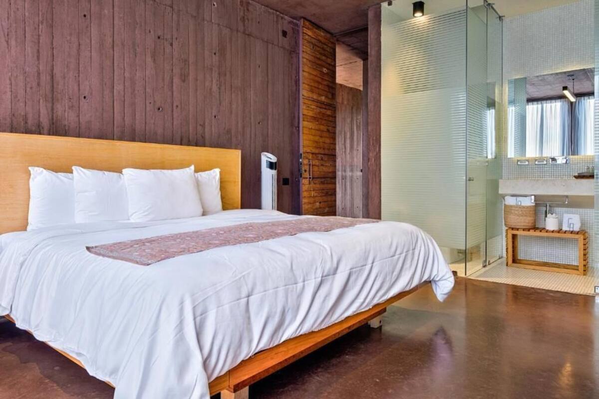 A bedroom with a wooden headboard, a large bed with white bedding, and a glass shower enclosure.