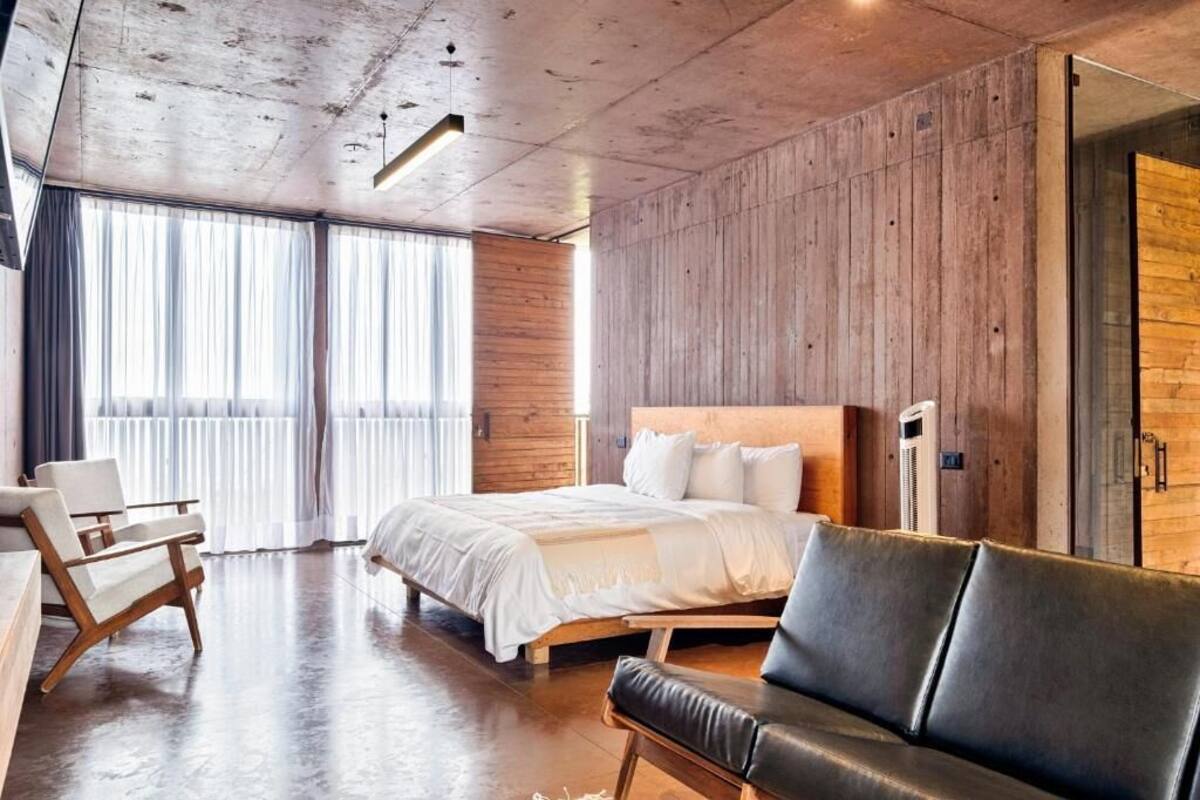 A modern hotel room with a large bed, a leather sofa, and wooden paneling on the walls.