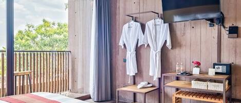 Une chambre avec un lit, un téléviseur fixé au mur, une petite table avec un vase et des bouteilles, et un balcon doté d’une balustrade en bois.