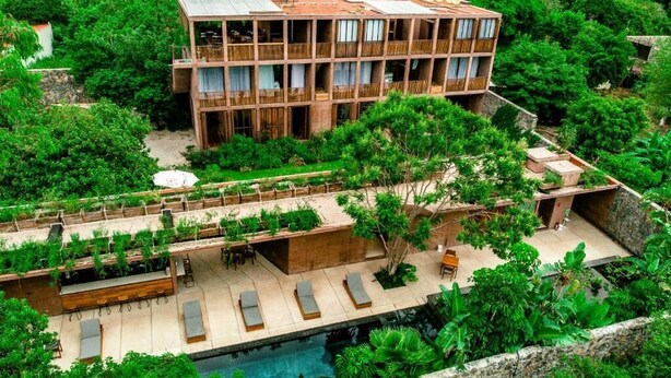 A multi-story building with balconies, a pool, and lush greenery surrounding it.