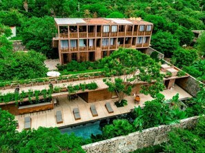 Um edifício com várias andares, varandas, piscina e vegetação exuberante ao redor.