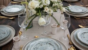 A table set for a formal outdoor dining event with white floral centerpieces, grey plates, and gold cutlery.