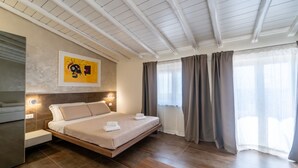 A modern hotel room with a bed, bedside tables, a painting, and a view of the outdoors. - giardini inn arte (Giardini Naxos)
