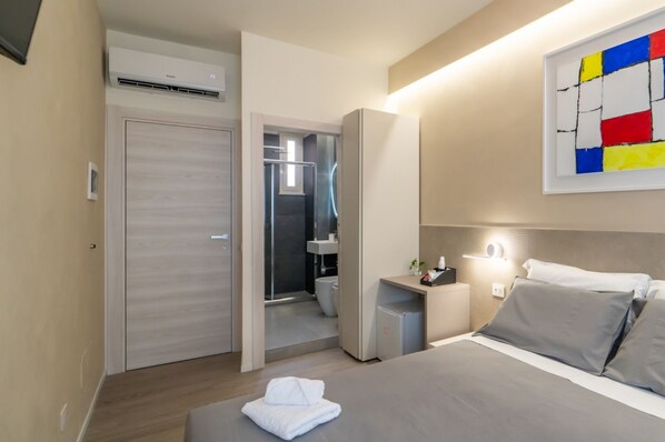 Une chambre d’hôtel moderne, équipée d’un lit, d’une table de chevet et d’une salle de bain visible à travers une porte ouverte.