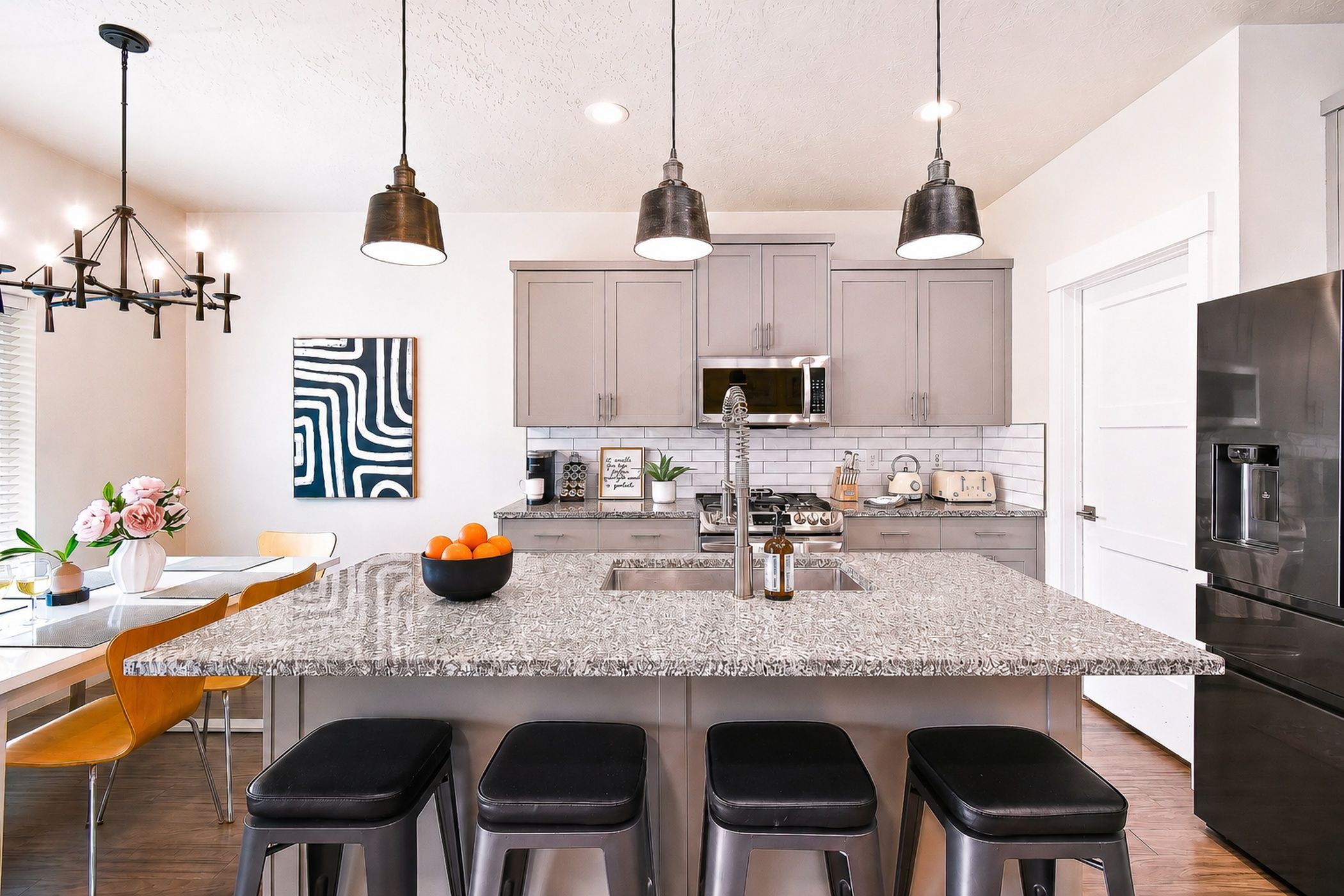 A modern kitchen with a central island, bar stools, pendant lighting, and stainless steel appliances.