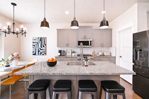 A modern kitchen with a central island, bar stools, pendant lighting, and stainless steel appliances. - 2 Adjacent Modern Homes • Sleep 16 • Near Top Shopping, Dining & Entertainment (Meridian)