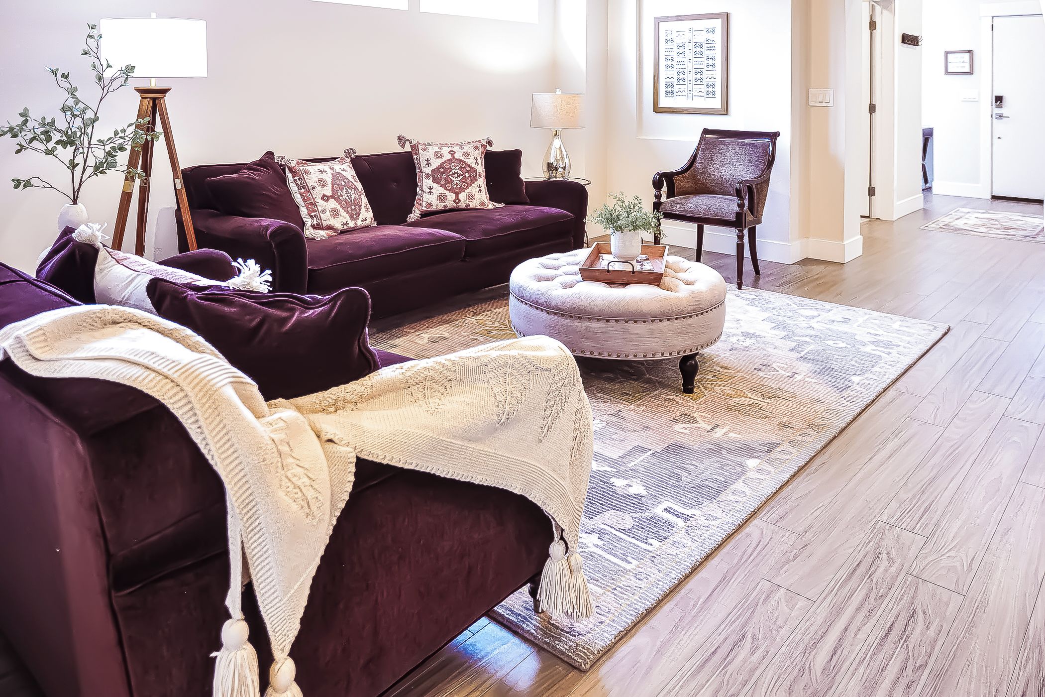 A living room with a dark purple sofa, a round ottoman, and a patterned rug.