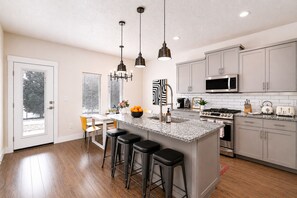 Una cocina moderna con una isla central, taburetes de bar, electrodomésticos de acero inoxidable e iluminación colgante.