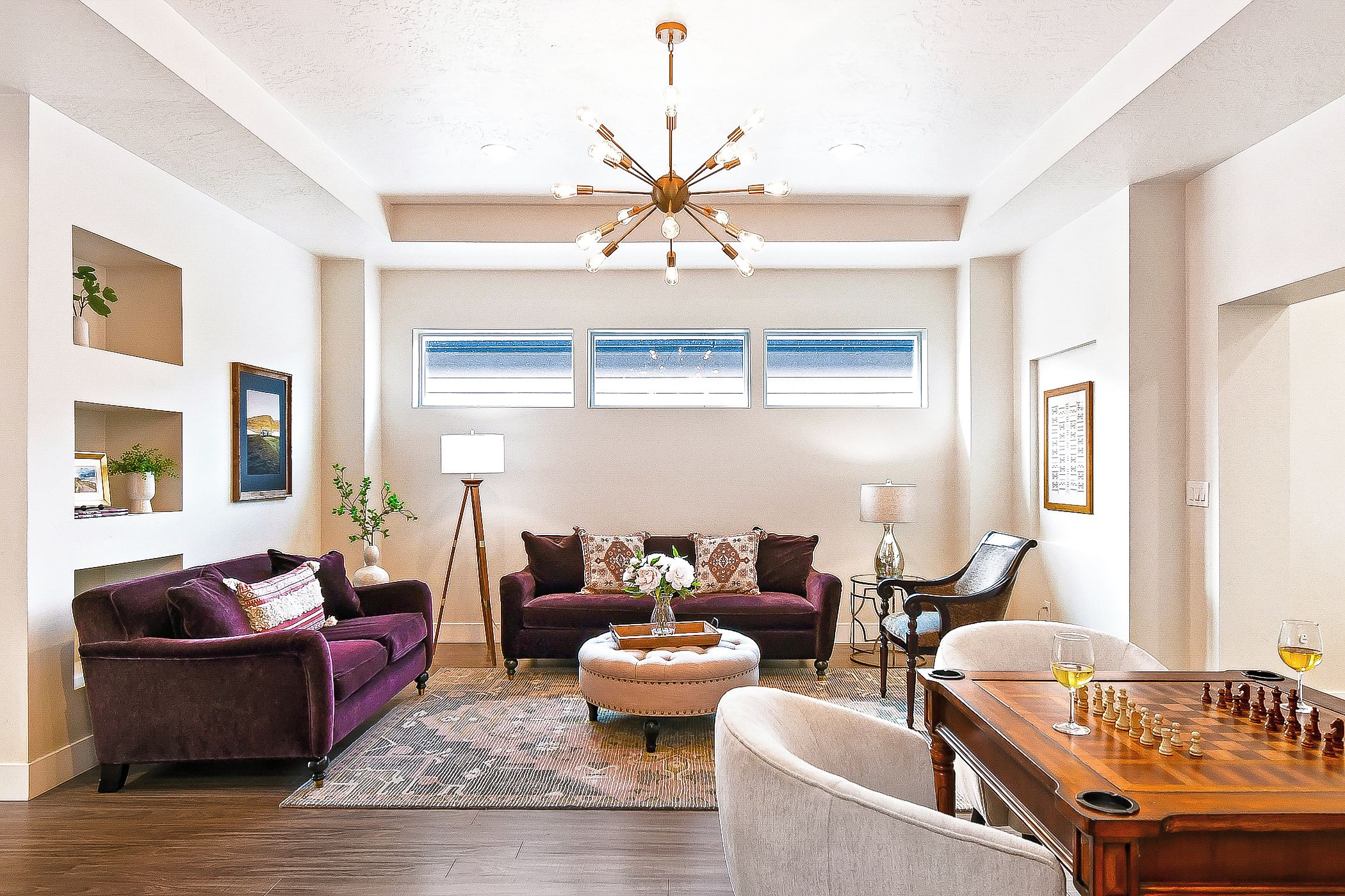 A spacious living room with a large wooden coffee table, two sofas, a chandelier, and a chess table.