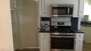 Une cuisine de taille réduite, avec des meubles blancs, un four à micro-ondes et une cuisinière.