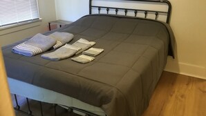 Un lit bien fait, avec une couette grise et plusieurs serviettes pliées.