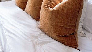A neatly made bed with white bedding and several brown pillows.