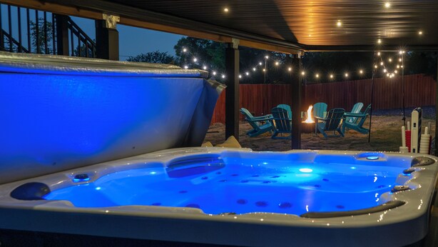 A hot tub with a blue light, surrounded by outdoor chairs and a string of lights.