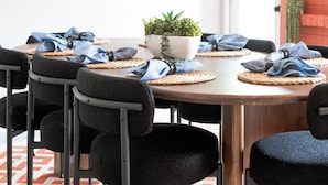 A dining area with a round table, black chairs, woven placemats, and a potted plant.
