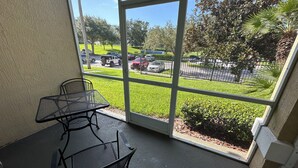 A balcony with a table and chairs, overlooking a parking lot and greenery. - Windsor Palms 3 bed ground floor condo near DISNEY! (Kissimmee)