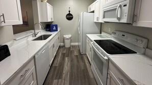 A compact kitchen with white cabinets, a stainless steel sink, a microwave, and a stove. - Windsor Palms 3 bed ground floor condo near DISNEY! (Kissimmee)