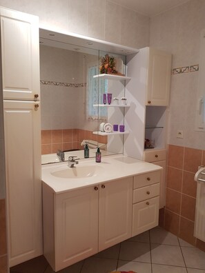 Une salle de bain avec un lavabo blanc, deux armoires, un miroir et une étagère contenant des articles de toilette.