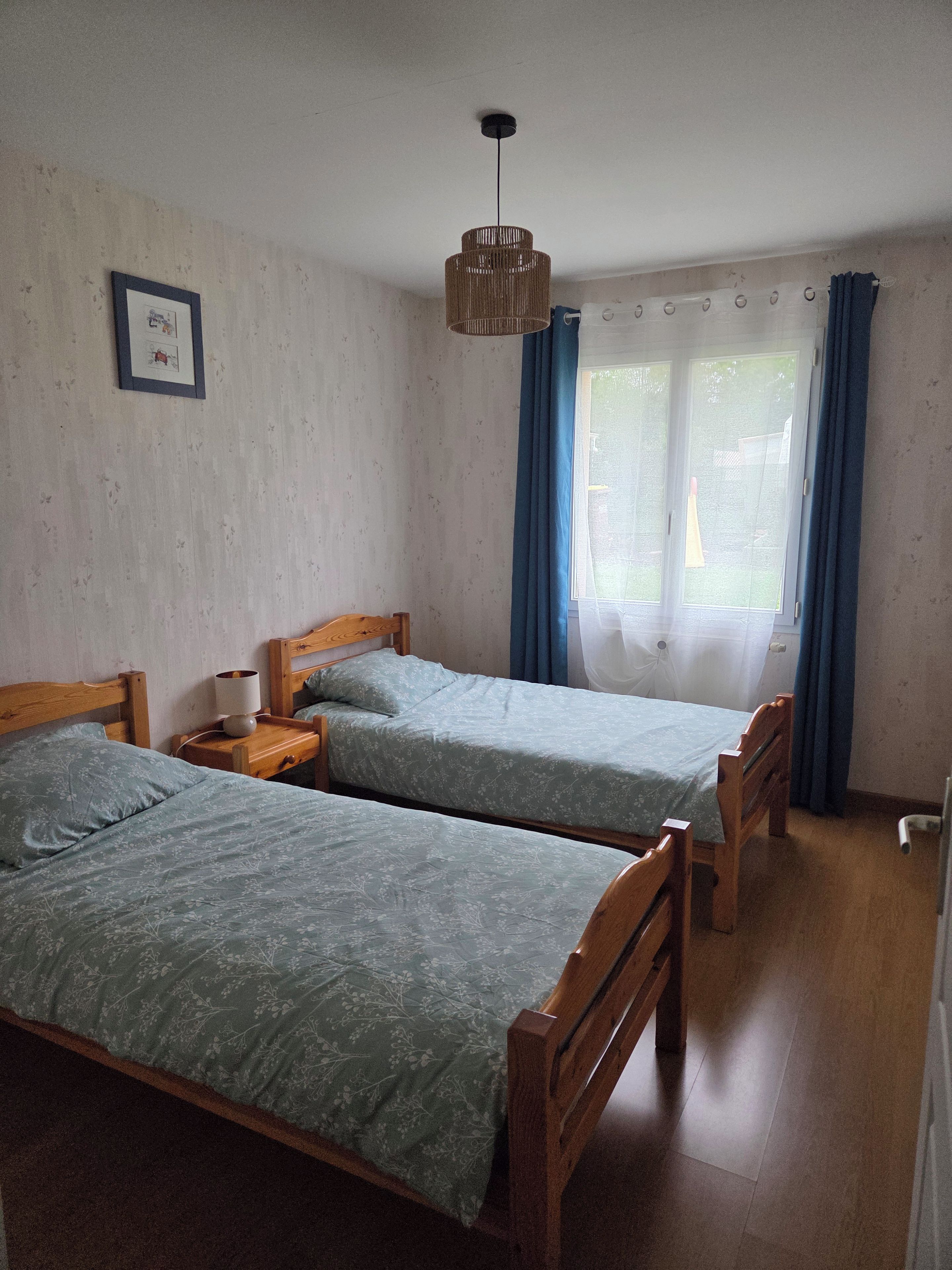 A room with two wooden beds, a hanging light fixture, and a window with curtains.