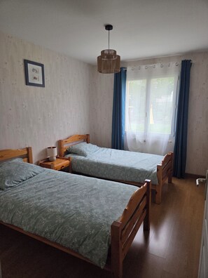 Une pièce avec deux lits en bois, un luminaire suspendu et une fenêtre avec des rideaux.
