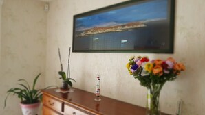 A room with a wooden dresser, a potted plant, a vase with flowers, and a framed picture on the wall.