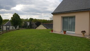 A house with a sloped roof, a large window with a curtain, and a well-maintained lawn.