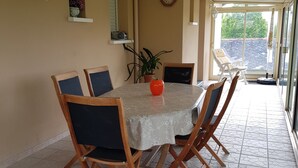 A dining area with a round table, six wooden chairs, a potted plant, and a wall clock.