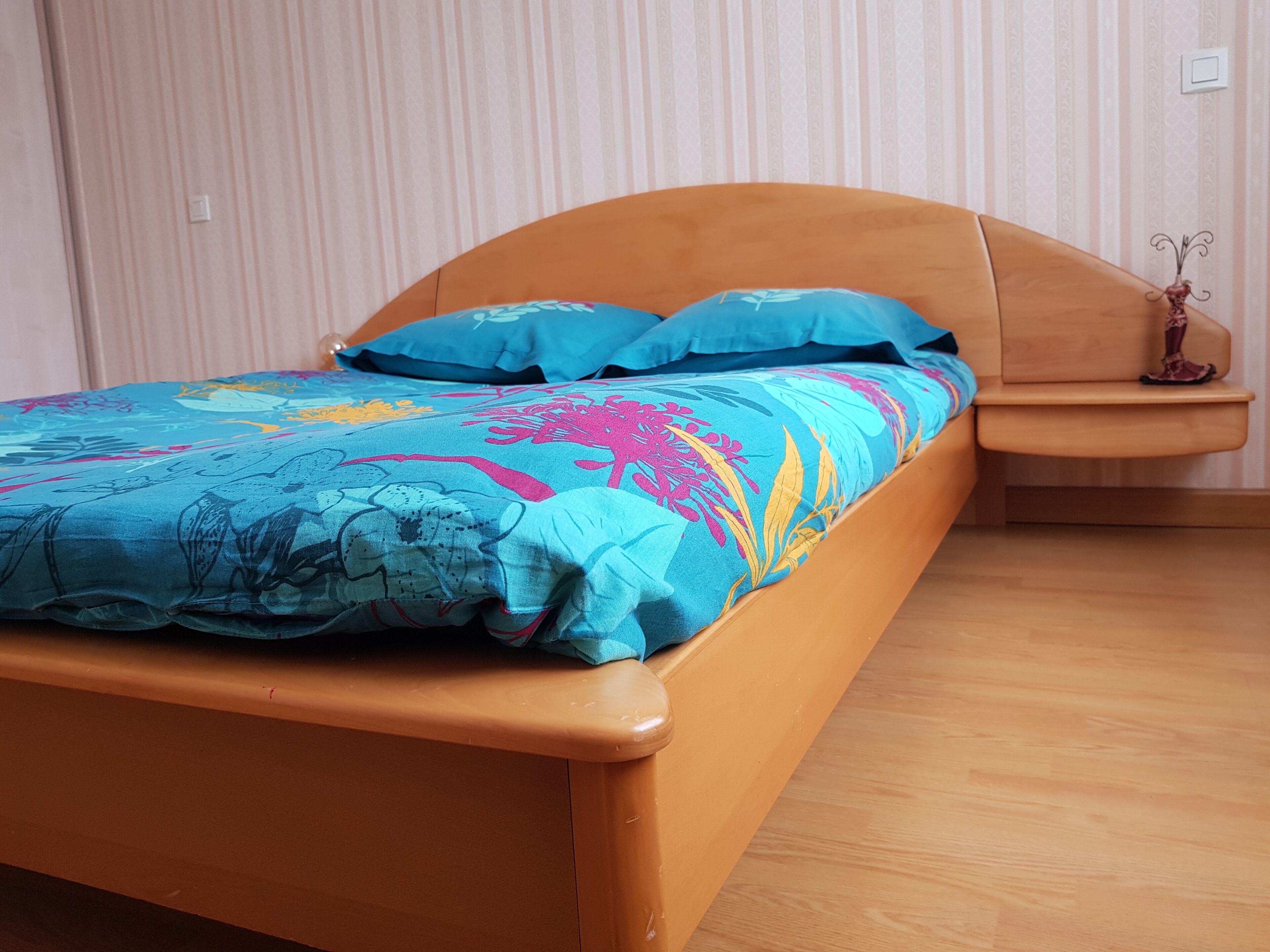 Een bed met een houten frame en een kleurrijke bloemenprint.