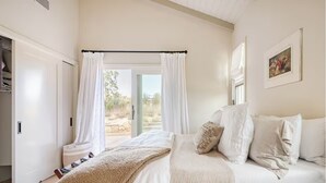 Un dormitorio con cama, cortinas blancas, una ventana y un cuadro en la pared.