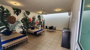 Une chambre avec deux lits, une table à manger, des chaises, un ventilateur de plafond et un réfrigérateur.