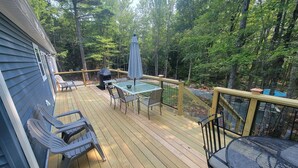 Eine Holzterrasse mit Gartenmöbeln, darunter Stühle und ein Tisch, umgeben von einem Wald.