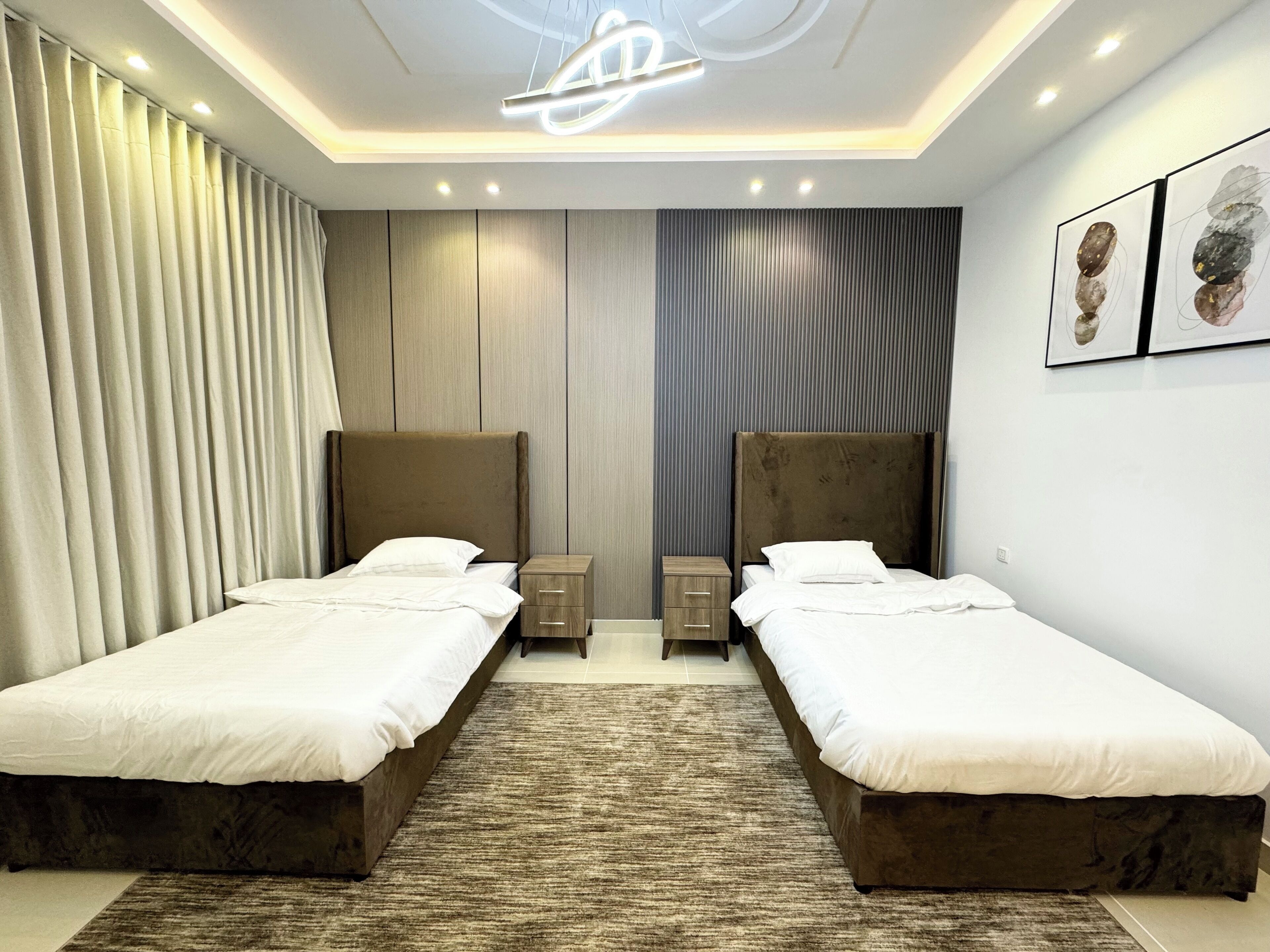 A modern hotel room with two beds, a large rug, and a unique ceiling light fixture.