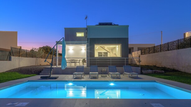 Une maison moderne dotée d’une piscine, d’un espace salon extérieur et d’une terrasse bien éclairée.