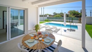 Un espace repas avec vue sur la piscine, comprenant une table ronde avec des chaises, une porte vitrée et une vue sur une piscine.