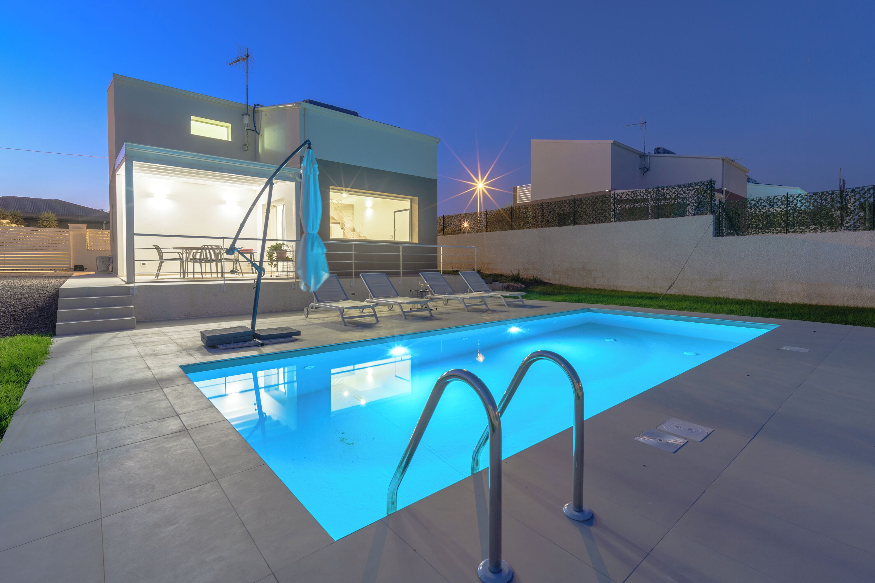 A modern house with a swimming pool, a covered patio, and a well-lit interior.