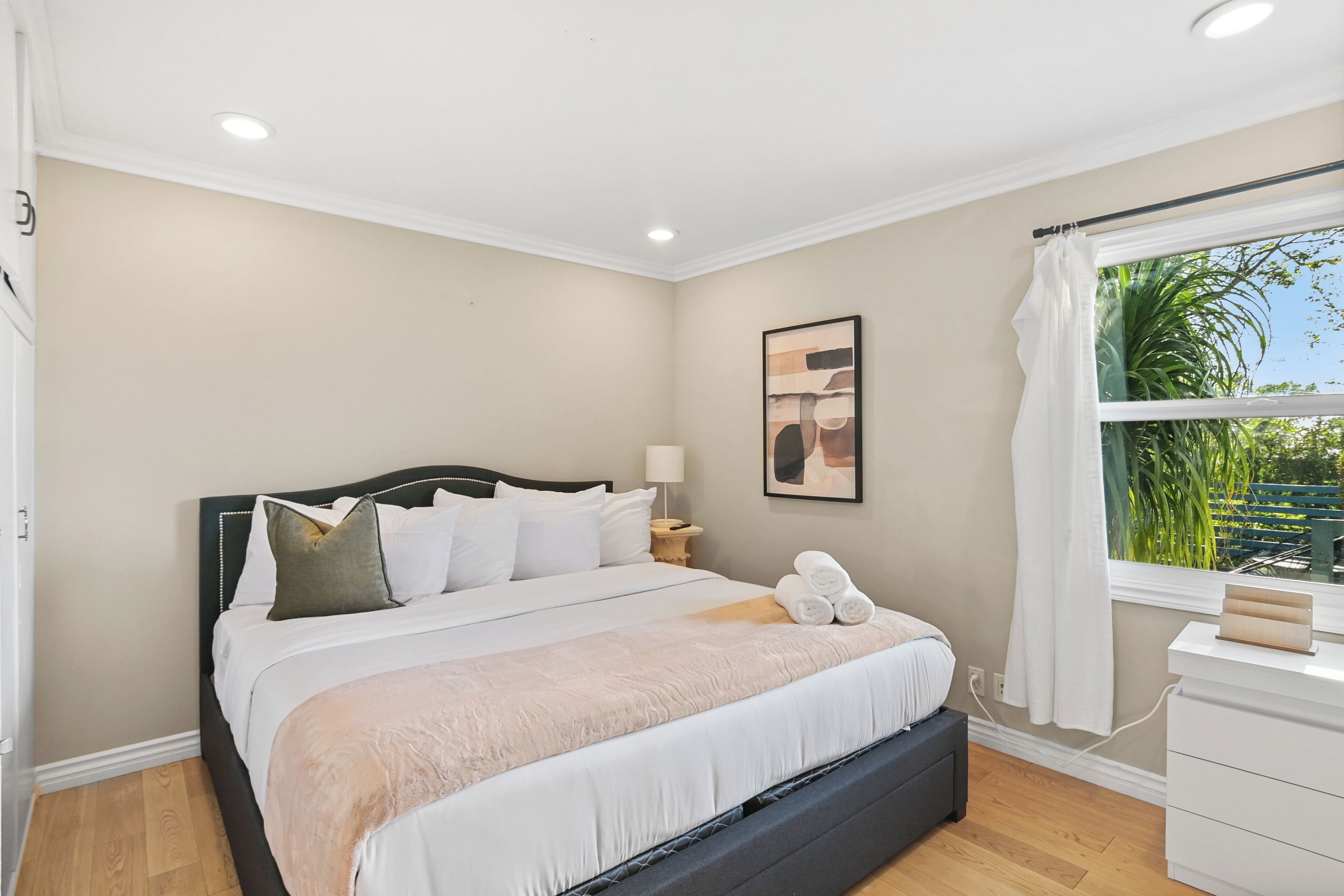 Un dormitorio con cama, mesita de noche, lámpara y ventana con cortinas.