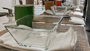 A dining table set with clear glassware, a green container, and a hanging plant. - Kimberly Surprise (Surprise)
