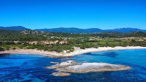 Una zona costiera con spiaggia, affioramenti rocciosi e montagne sullo sfondo.