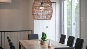 A dining area with a wooden table, chairs, a hanging rattan light fixture, and a potted plant. - La Vue O-Lac Magog (Sherbrooke)