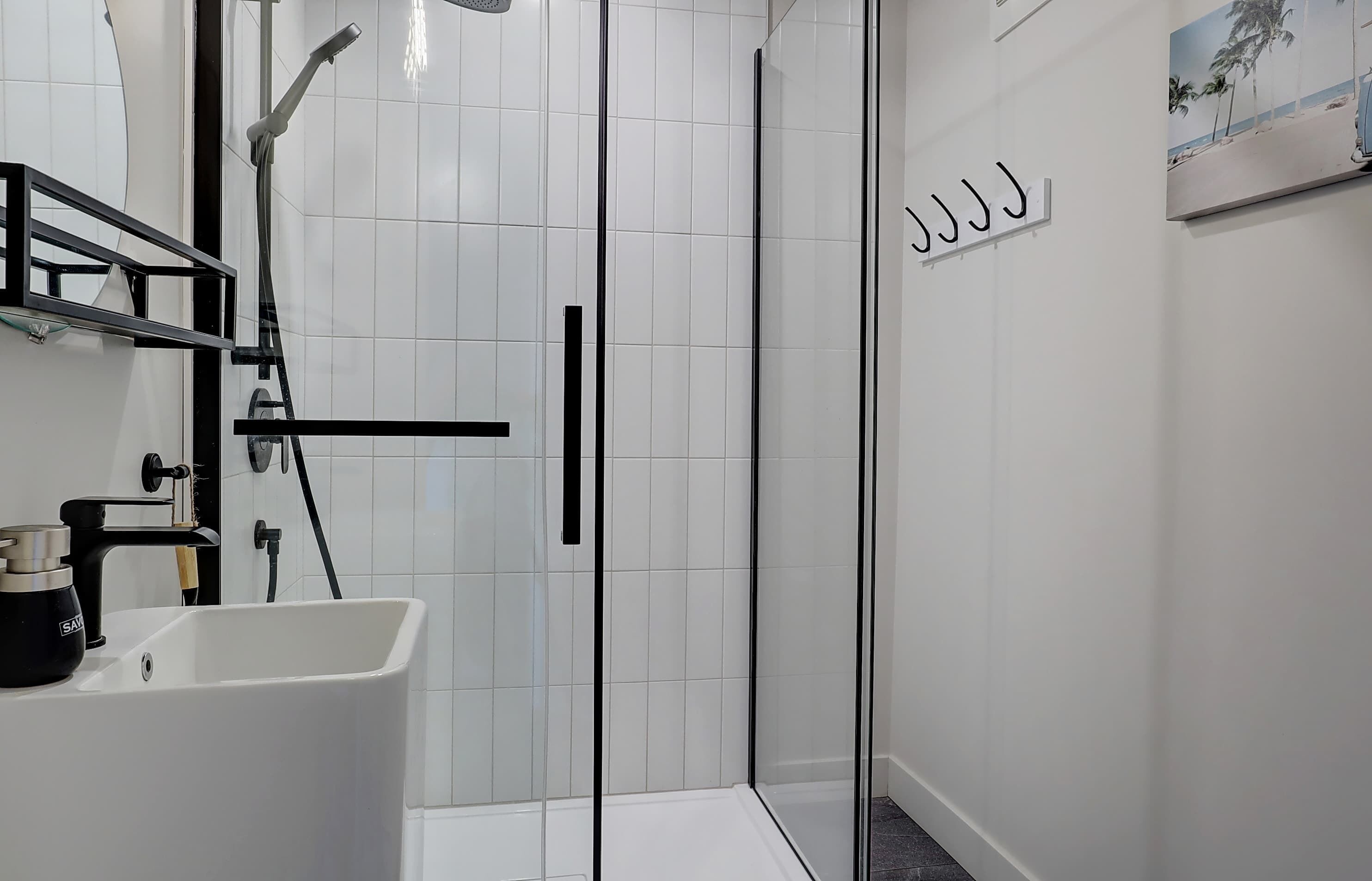 A modern bathroom with a glass-enclosed shower, a white sink, and a black towel holder.