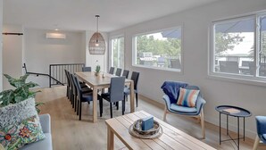 A modern dining area with a wooden table and chairs, a hanging light fixture, and large windows offering views of the outdoors. - La Vue O-Lac Magog (Sherbrooke)