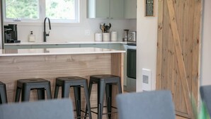A modern kitchen with a wooden island, bar stools, and a view of the outdoors. - La Vue O-Lac Magog (Sherbrooke)