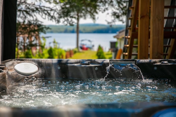 A hot tub with water splashing, surrounded by greenery and a view of a lake.