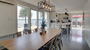 Eine moderne Küche mit großen Fenstern, einem Essbereich mit einem langen Tisch und Blick auf den See.
