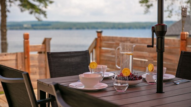 Eine Holzterrasse mit einem für eine Mahlzeit gedeckten Tisch, mit Blick auf ein Gewässer.