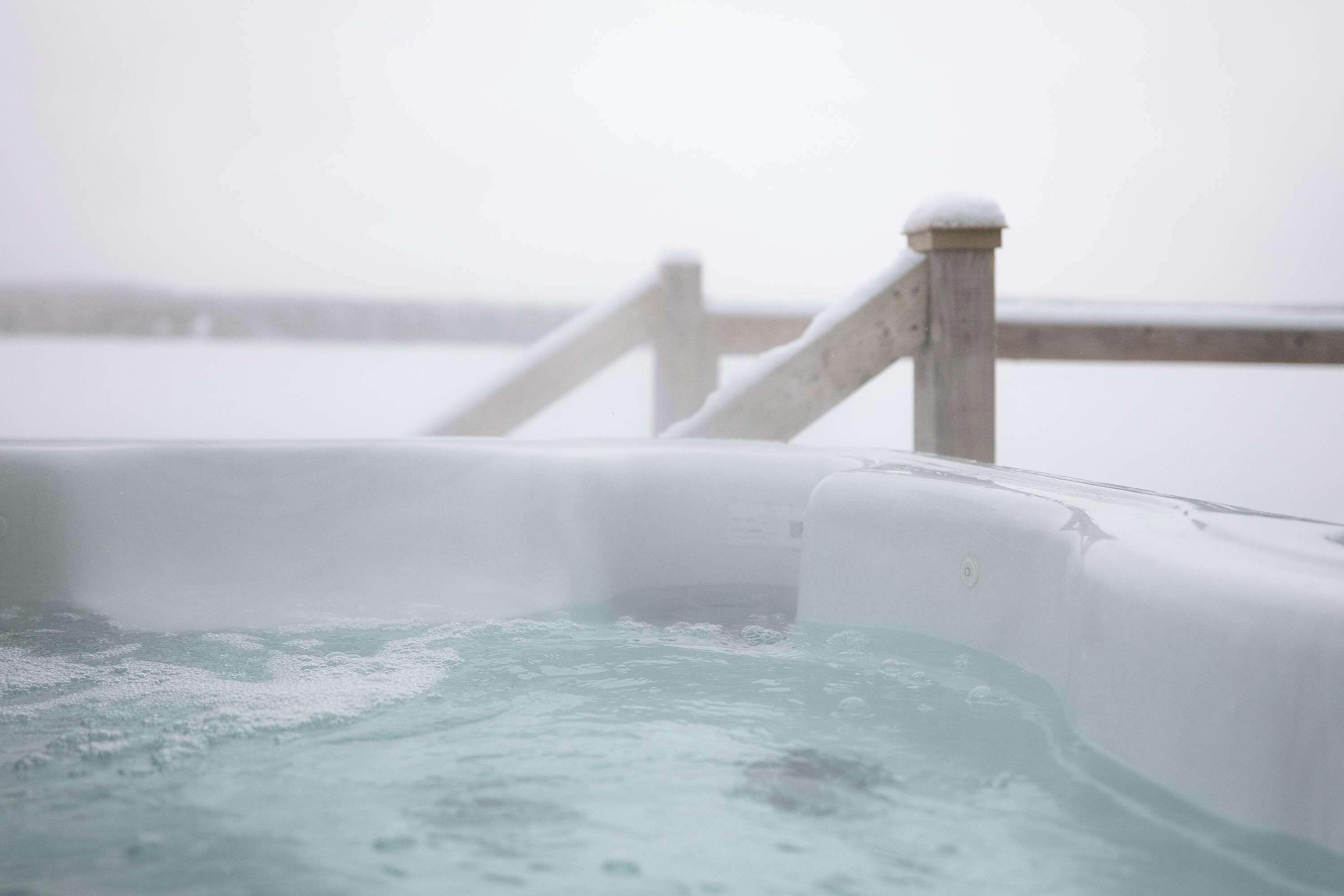 A hot tub with a wooden railing and a snowy background.